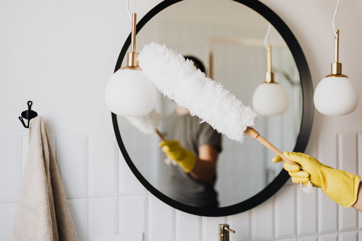 Dépoussiérage d’un luminaire devant un miroir, à la lumière du jour